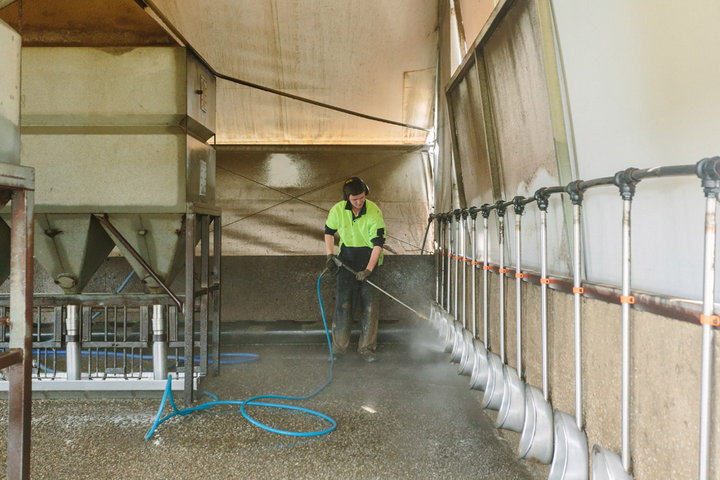 Farm worker hosing the inside of a pig shed