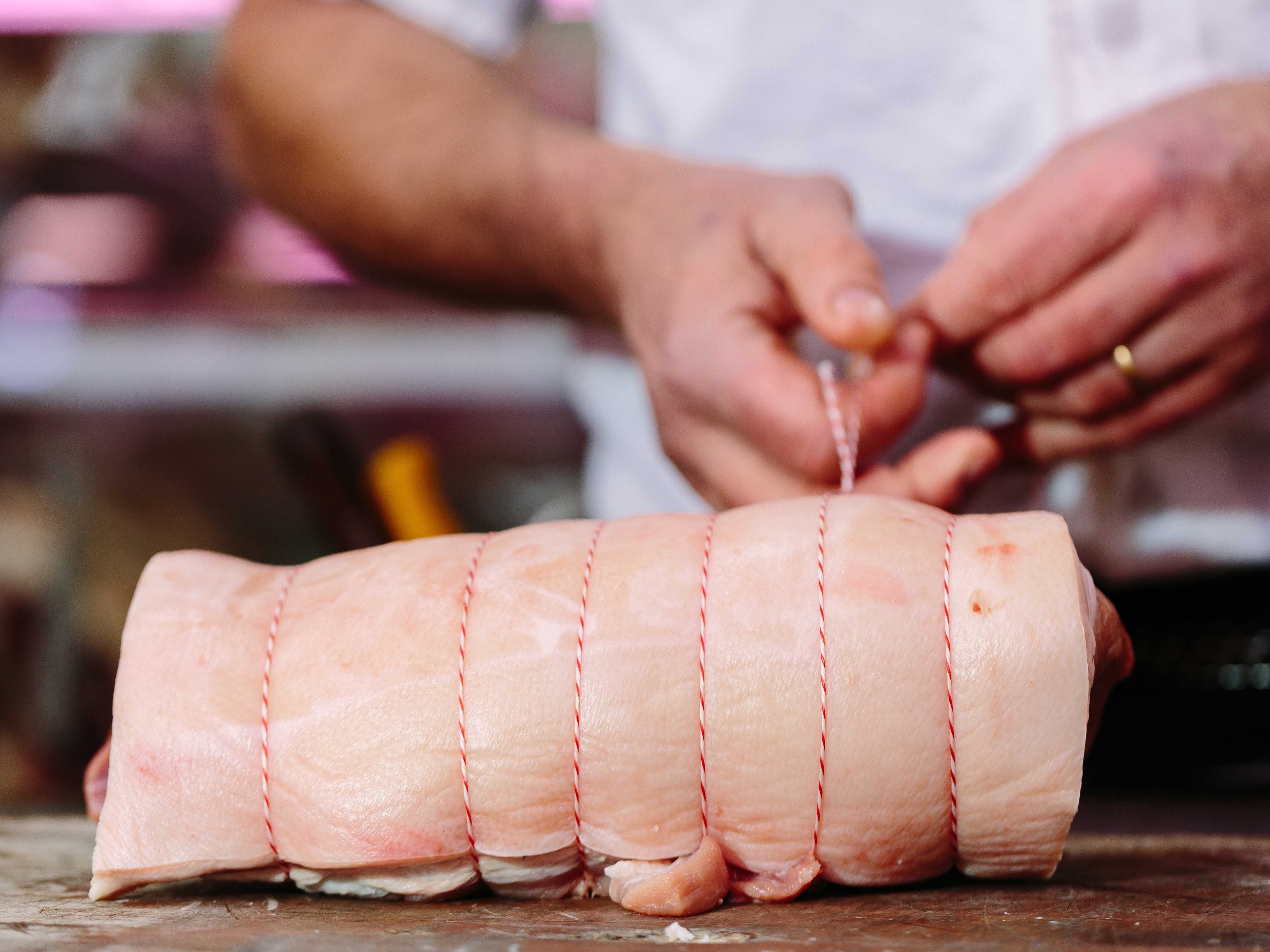 A butcher wrapping twine around a pork roast. Close up, can only see butcher's hands and pork.